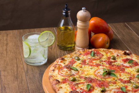 Photo for Pizza Marguerita made with tasty pizza dough, Mozzarella, tomatoes, marjoram and green olives. On the wooden board. Napolitan Pizza. Sparkling water Lemon and ice cubes. Gastronomic photography left - Royalty Free Image