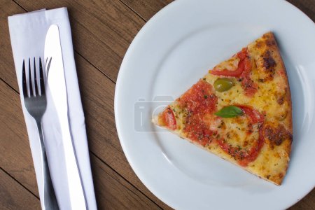 Foto de Pizza Marguerita elaborada con Queso Mozzarella, tomates, hojas de albahaca y aceitunas verdes. Rebanada de pizza servida en plato blanco. Agua con gas y limones. Foto gourmet - Imagen libre de derechos