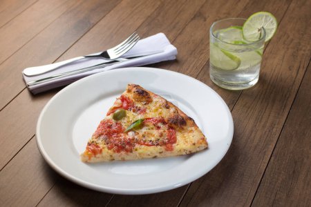 Photo for Gastronomic Photography of Pizza Marguerita made with Mozzarella Cheese, tomatoes, basil leaves and green olives. Pizza slice served on white plate. Sparkling water and lemons. Made in the wood oven. - Royalty Free Image