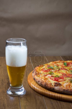 Foto de Pizza Marguerita elaborada con Queso Mozzarella, tomates, hojas de albahaca y aceitunas verdes. Un vaso de cerveza. Combinación perfecta para tus momentos felices. Espacio superior para escribir. - Imagen libre de derechos