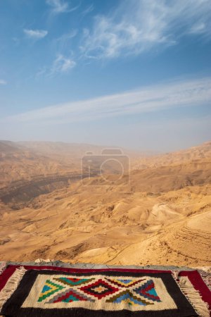 Téléchargez les photos : Vue panoramique du canyon de Mujib, Jordanie du point de vue du panorama de Moujib avec tapis bédouin contre ciel bleu avec nuages - en image libre de droit