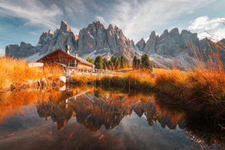 Foto de Vista panorámica de Geisler Alm Rifugio delle Odle frente a las montañas de dolomitas y reflexión en el agua de un estanque, Tirol del Sur, Italia - Imagen libre de derechos