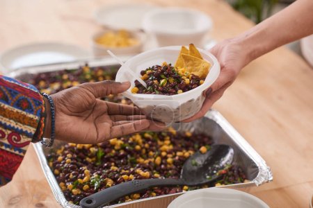 Téléchargez les photos : Volontaire méconnaissable donnant bol en plastique avec déjeuner repas aux pauvres dans la cantine de charité moderne - en image libre de droit