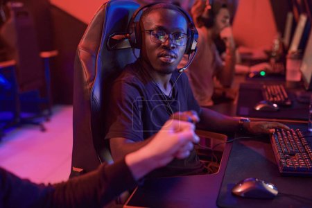 Photo for African-American gamer in headphones making fist bump with team member while they playing video game in esports tournament - Royalty Free Image