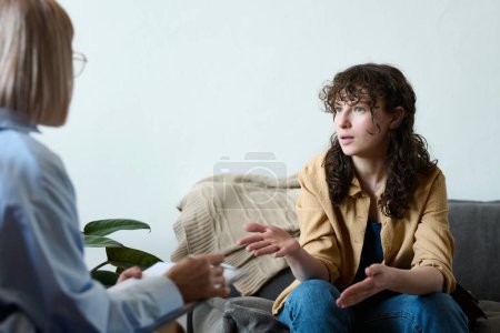 Photo for Young woman having consultation with psychologist, they sitting opposite each other and discussing problems - Royalty Free Image