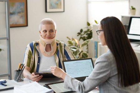 Foto de Mujer con lesión de cuello visitando a la compañía de seguros para firmar documentos con el agente - Imagen libre de derechos