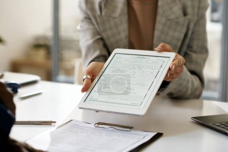 Primer plano de la mujer de negocios que muestra el contrato en la tableta PC al cliente durante la reunión en el cargo