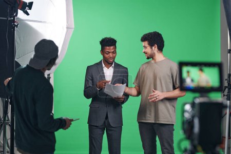 Photo for African American presenter discussing script with director while they standing in professional studio - Royalty Free Image