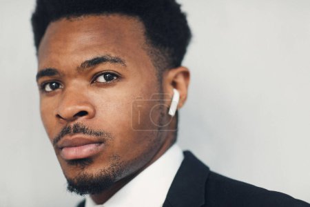 Foto de Primer plano del joven empresario afroamericano serio usando auriculares Bluetooth para la comunicación en movimiento - Imagen libre de derechos