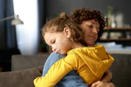 Junge Mutter umarmt und beruhigt ihr Kind, während es schlechte Laune hat oder Gefühle weckt