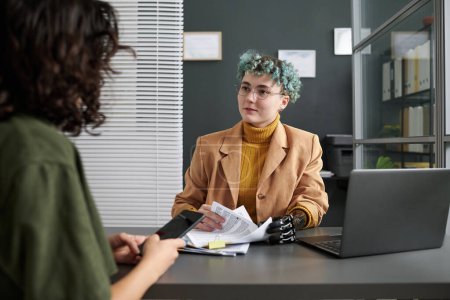 Foto de Mujer joven con prótesis hablando con el cliente y discutiendo documentos mientras se reúnen en la oficina - Imagen libre de derechos