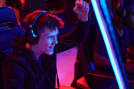 Photo for Happy young Caucasian man in headphones making yes gesture while winning game during esports competition - Royalty Free Image