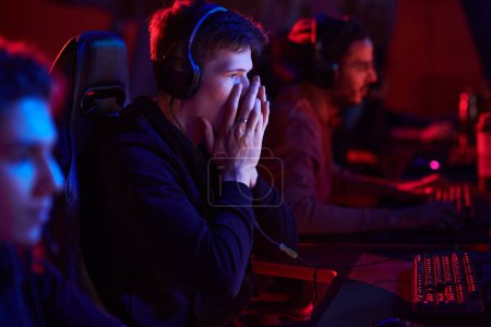 Photo for Shocked teenage gamer in headphones covering mouth and looking at monitor while losing game at esports tournament - Royalty Free Image