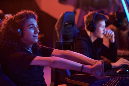 Téléchargez les photos : Contenu jeune joueur d'ordinateur caucasien avec de longs cheveux bouclés étirant les doigts avant la compétition d'esport - en image libre de droit
