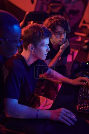 Photo for Concentrated young gamers sitting in neon room and brainstorming about strategy of video game - Royalty Free Image
