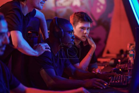 Photo for Concentrated young multi-ethnic gamers of esports team analyzing tactic of game while playing game in computer club - Royalty Free Image