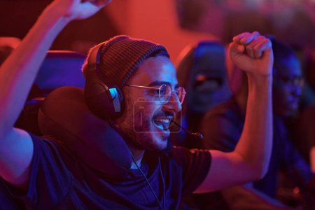 Photo for Cheerful young mixed race man in headset with microphone making yes gesture while celebrating winning in game - Royalty Free Image