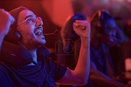 Photo for Emotional young mixed race esports gamer with stubble looking up and making yes gesture in computer club - Royalty Free Image