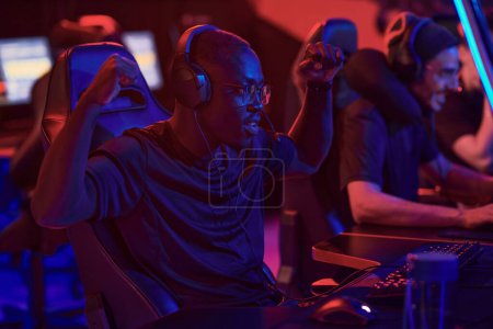 Photo for Positive young Black guy in headphones gesturing hands like monkey while winning game, he participating in esports championship - Royalty Free Image