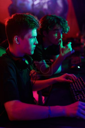 Téléchargez les photos : Équipe de joueurs de cybersport regardant l'écran d'ordinateur et analysant les tactiques de jeu en ligne, lumière rouge - en image libre de droit