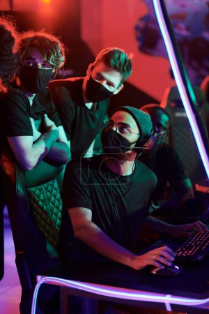 Photo for Group of young cybersports gamers in black masks chatting about strategy of game while participating in esports competition - Royalty Free Image