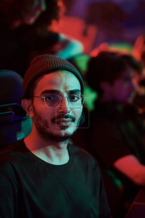 Téléchargez les photos : Portrait de contenu jeune joueur arabe dans des lunettes participant à la ligue de sport électronique, lumière au néon - en image libre de droit