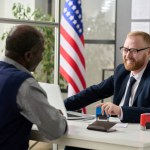 Portrait of friendly smiling worker consulting senior black man in US immigration office