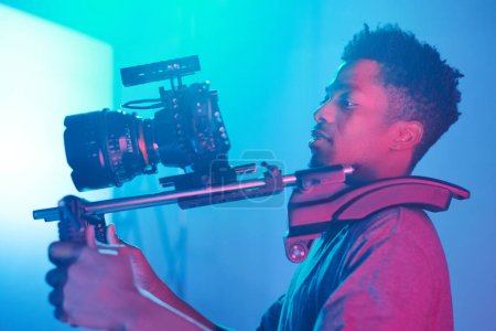 Junge afroamerikanische professionelle Betreiber, die Videoinhalte mit speziellem Gerät und professioneller Kamera erstellen