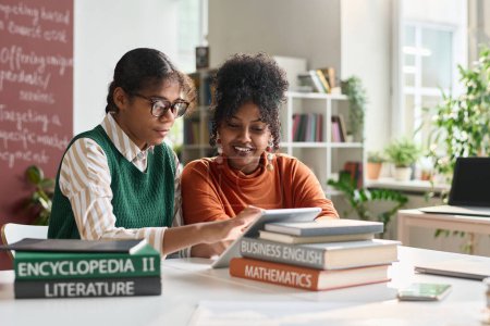 Téléchargez les photos : Portrait de deux jeunes filles noires utilisant une tablette numérique dans la classe de l'école et travaillant sur l'espace de copie de présentation en ligne - en image libre de droit