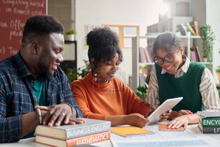 Téléchargez les photos : Groupe de jeunes afro-américains étudiant ensemble dans une salle de classe collégiale et utilisant une tablette numérique travaillant sur la présentation en ligne - en image libre de droit