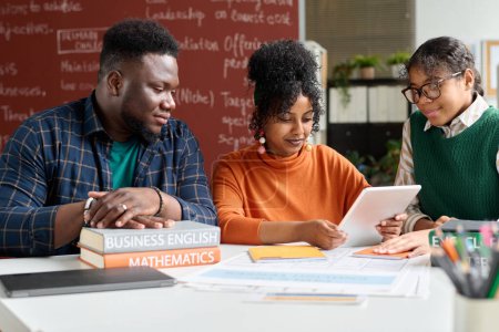 Téléchargez les photos : Jeunes noirs utilisant une tablette numérique dans la salle de classe du collège et travaillant ensemble sur la présentation en ligne - en image libre de droit