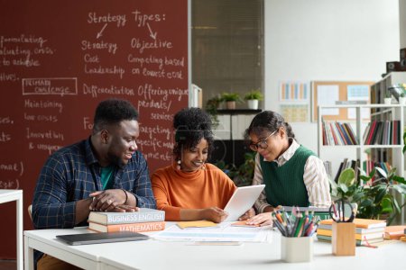 Foto de Grupo de tres adolescentes afroamericanos disfrutando de trabajar juntos en el aula universitaria y usando tableta digital - Imagen libre de derechos