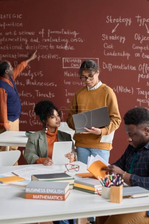 Foto de Retrato vertical de estudiantes universitarios afroamericanos haciendo estudios en grupo en el aula de la universidad con pizarra en el fondo - Imagen libre de derechos