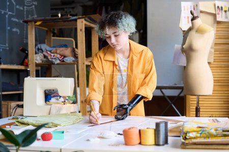 Photo for Waist up portrait of teenage girl with prosthetic arm sewing clothes in inclusive atelier workshop copy space - Royalty Free Image