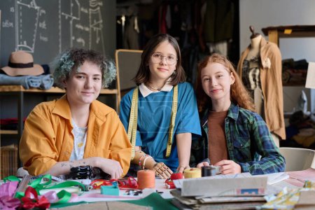 Photo for Inclusive group of three girls smiling at camera enjoying tailoring class in atelier workshop - Royalty Free Image