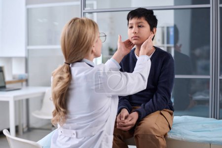 Rückenansicht einer Ärztin, die Hals und Rachen eines kleinen Jungen während eines Gesundheitschecks in einer Kinderklinik untersucht