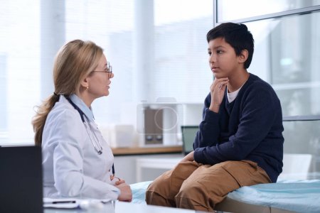 Side view portrait of young Middle Eastern boy talking to female doctor in pediatric clinic