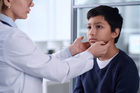 Portrait of young Middle Eastern boy in hospital with doctor examining neck and throat during checkup