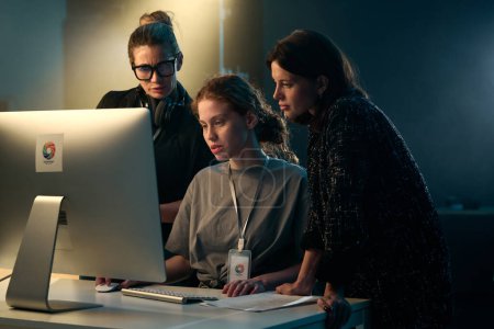 Minimale Aufnahme von drei Frauen, die gemeinsam auf einem Videoproduktionsset mit Hintergrundbeleuchtung auf den Computerbildschirm schauen