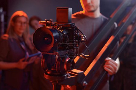 Nahaufnahme eines Kameramanns, der eine Videokamera auf einem Stativ im Studio mit roten Neonlichtern bedient
