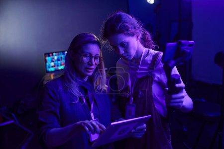 Portrait of female video production crew working together in dark purple light