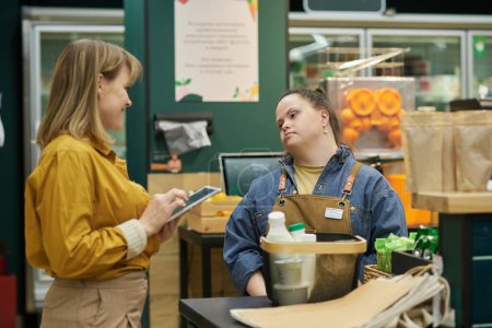Waist up portrait of young woman with disability working in supermarket with manager assisting and giving instructions