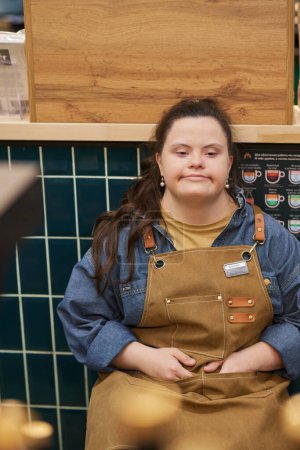 Vertical portrait of young woman with Down syndrome working in cafe and taking break sitting on chair