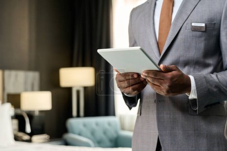 Primer plano del gerente de hotel de lujo afroamericano sosteniendo la tableta digital de pie en el espacio de copia de la habitación de hotel