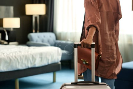 Acercamiento de una mujer negra irreconocible que entra en la habitación del hotel y sostiene la maleta al viajar al espacio de copia del resort