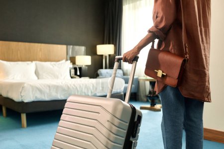 Vista trasera recortada de la mujer afroamericana que entra en la habitación del hotel y sostiene el espacio de copia de la maleta