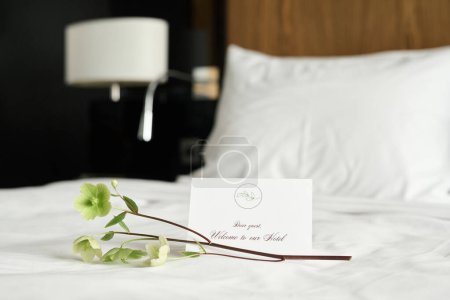 Background image of welcome note with delicate flower decor on bed in luxury in hotel room copy space