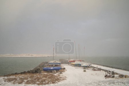 Téléchargez les photos : Voiliers situés sur un quai enneigé près de la mer froide contre un ciel gris nuageux en hiver - en image libre de droit