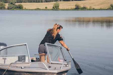 Téléchargez les photos : Femme avec pagaie en bateau à moteur sur la rivière par une journée ensoleillée - en image libre de droit