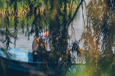 Photo for Blurred fishermen in boat behind hanging willow branches - Royalty Free Image